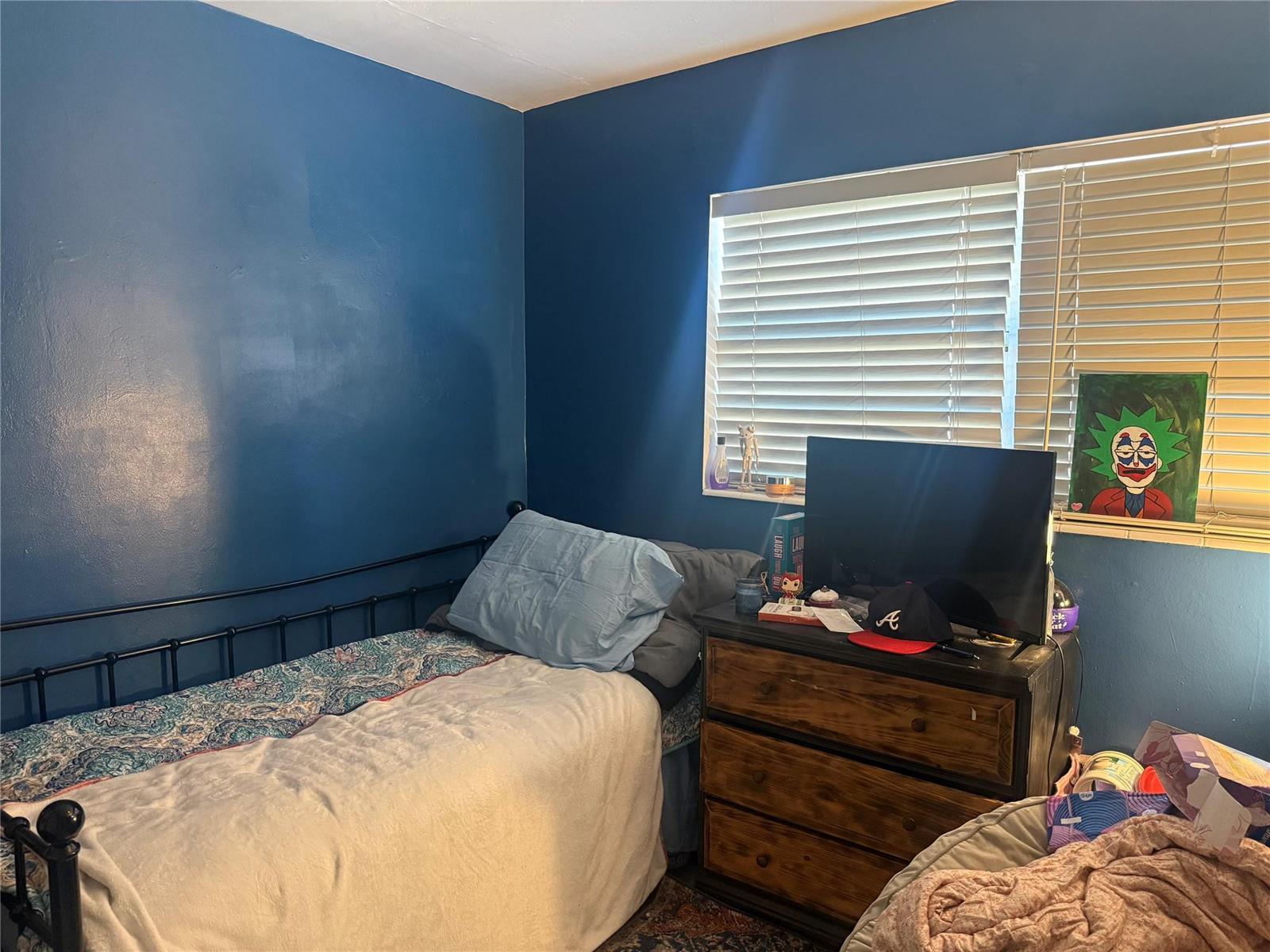 A bedroom with blue walls, a metal bed frame, a wooden dresser, and a window — 817 SE 9th Street, Okeechobee FL 34974, OKEECHOBEE, FL