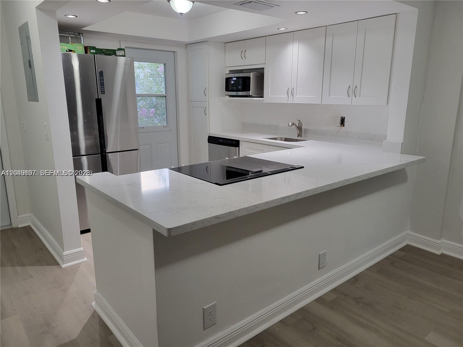 A modern kitchen features white cabinets, stainless steel appliances, and a white quartz peninsula countertop — 1333 E Hallandale Beach Blvd # 329, Hallandale Beach FL 33009, HALLANDALE BEACH, FL