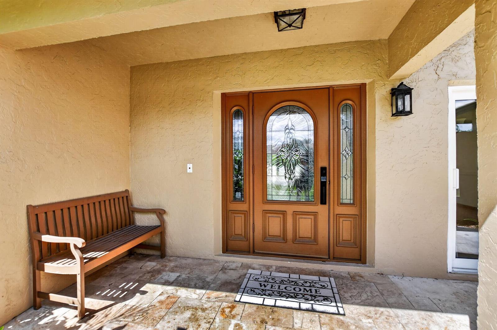 A wooden bench sits on a tiled porch in front of a decorative wooden door — 20876 Sugarloaf Lane, Boca Raton FL 33428, BOCA RATON, FL