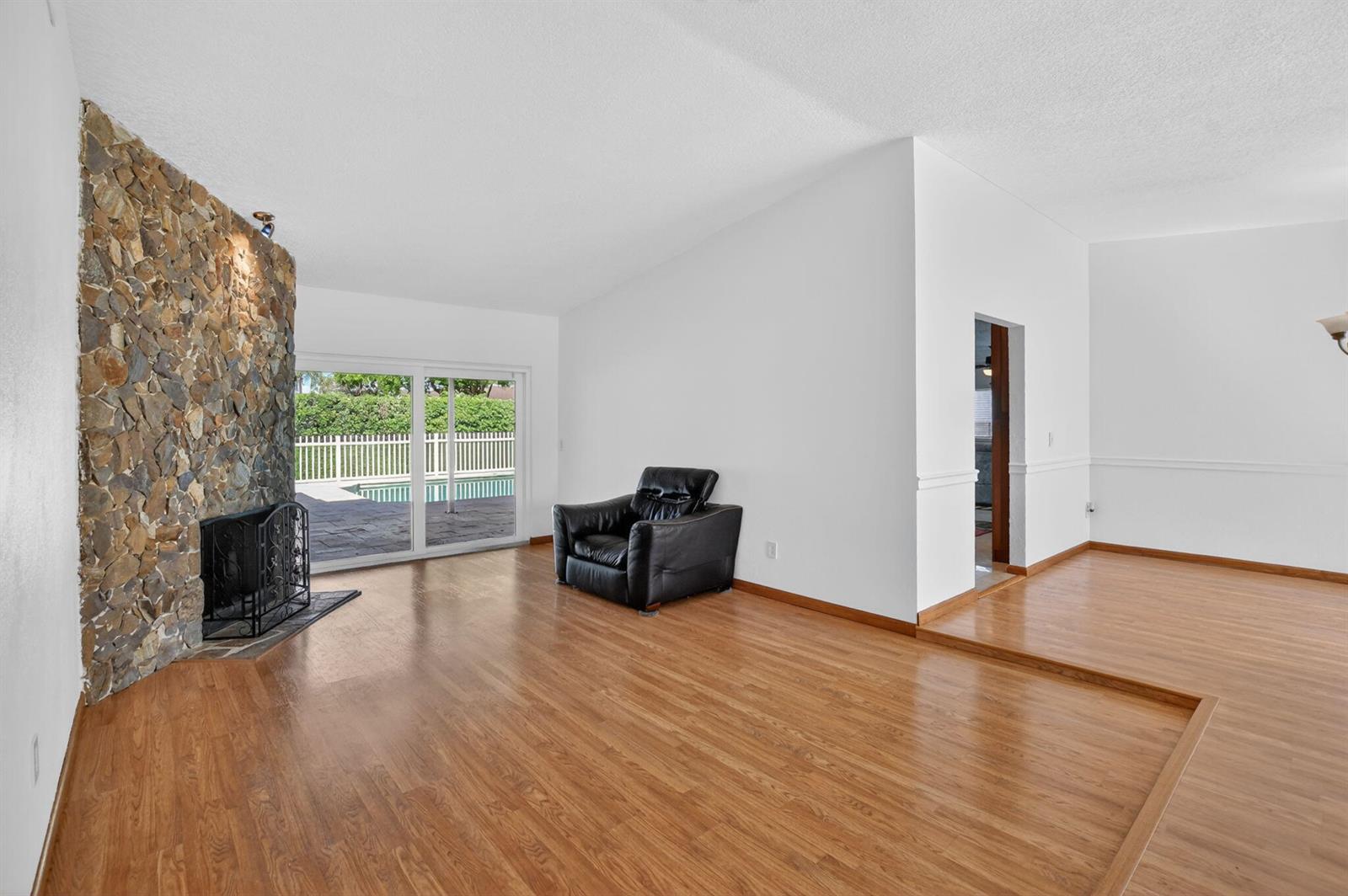 A living room features a stone fireplace, wood flooring, a black armchair, and sliding glass doors — 20876 Sugarloaf Lane, Boca Raton FL 33428, BOCA RATON, FL