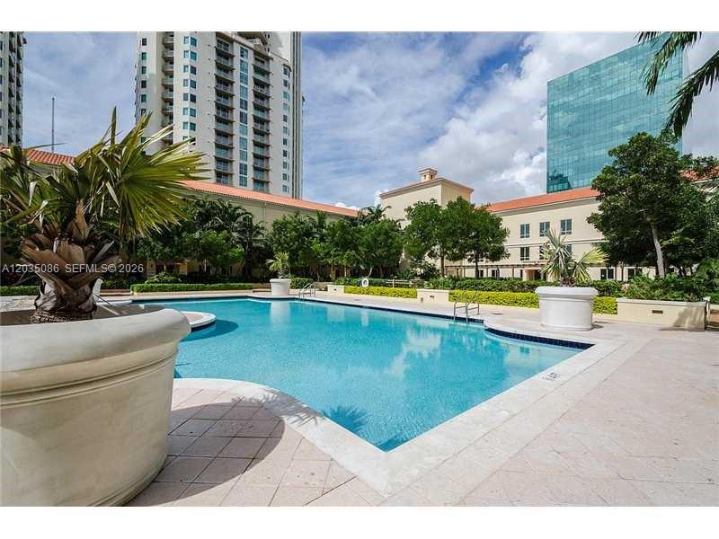 A swimming pool sits in a courtyard surrounded by buildings and potted palm trees — 7350 SW 89th St # 505S, Miami FL 33156, MIAMI, FL