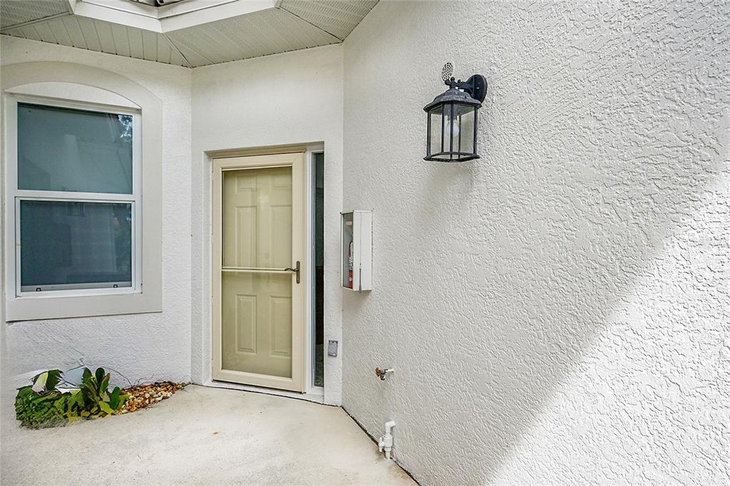 An exterior view of a home entrance with a storm door, light fixture, and stucco wall — 4700 YACHT HARBOR DRIVE UNIT 612, NAPLES, FL