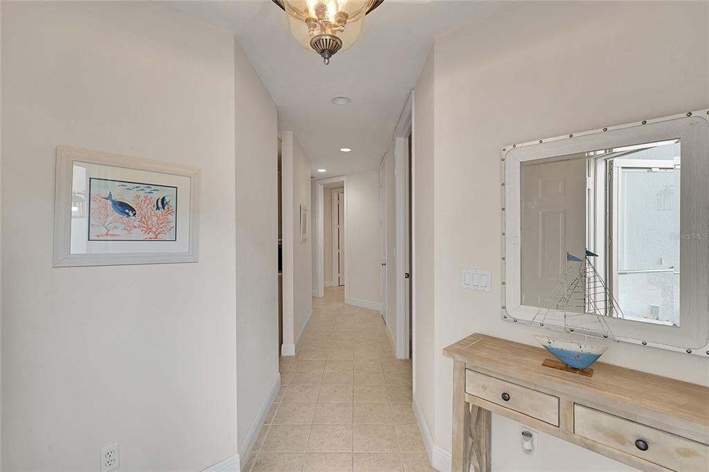 A hallway with tile flooring, a console table, a mirror, and framed nautical artwork — 4700 YACHT HARBOR DRIVE UNIT 612, NAPLES, FL