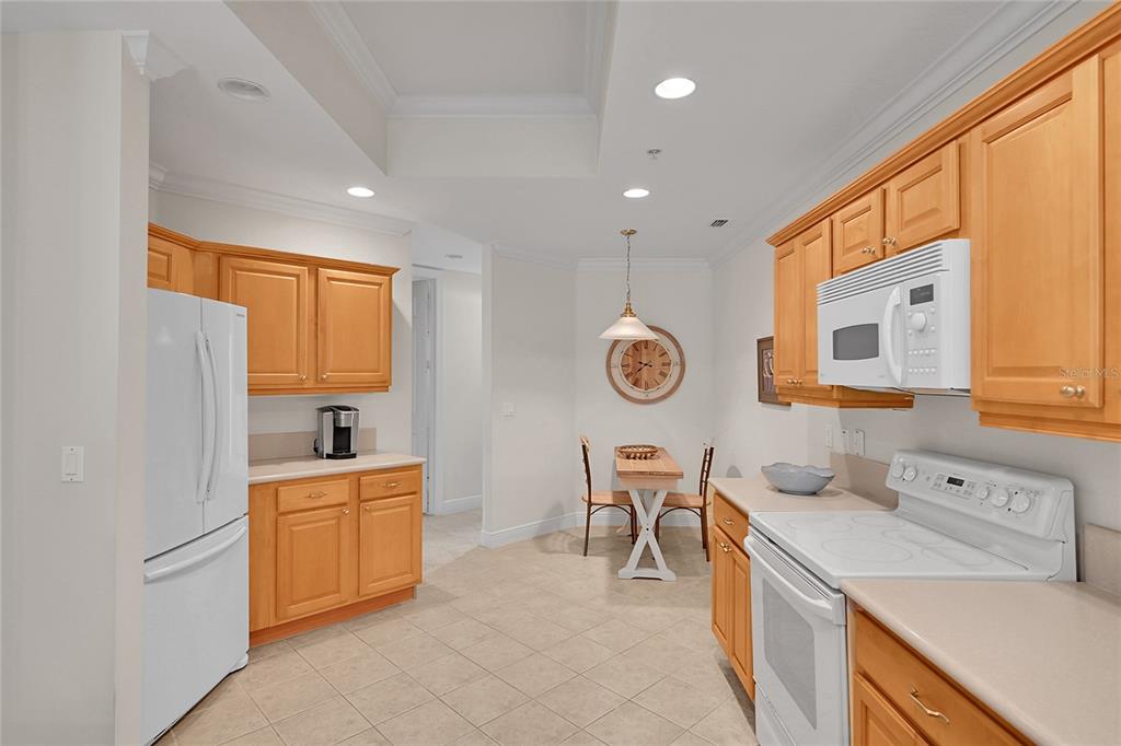 A kitchen with light wood cabinets, white appliances, tile flooring, and a small dining area — 4700 YACHT HARBOR DRIVE UNIT 612, NAPLES, FL