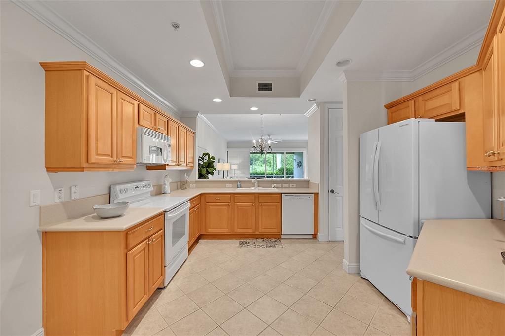 A kitchen with light wood cabinets, white appliances, and beige tile flooring — 4700 YACHT HARBOR DRIVE UNIT 612, NAPLES, FL