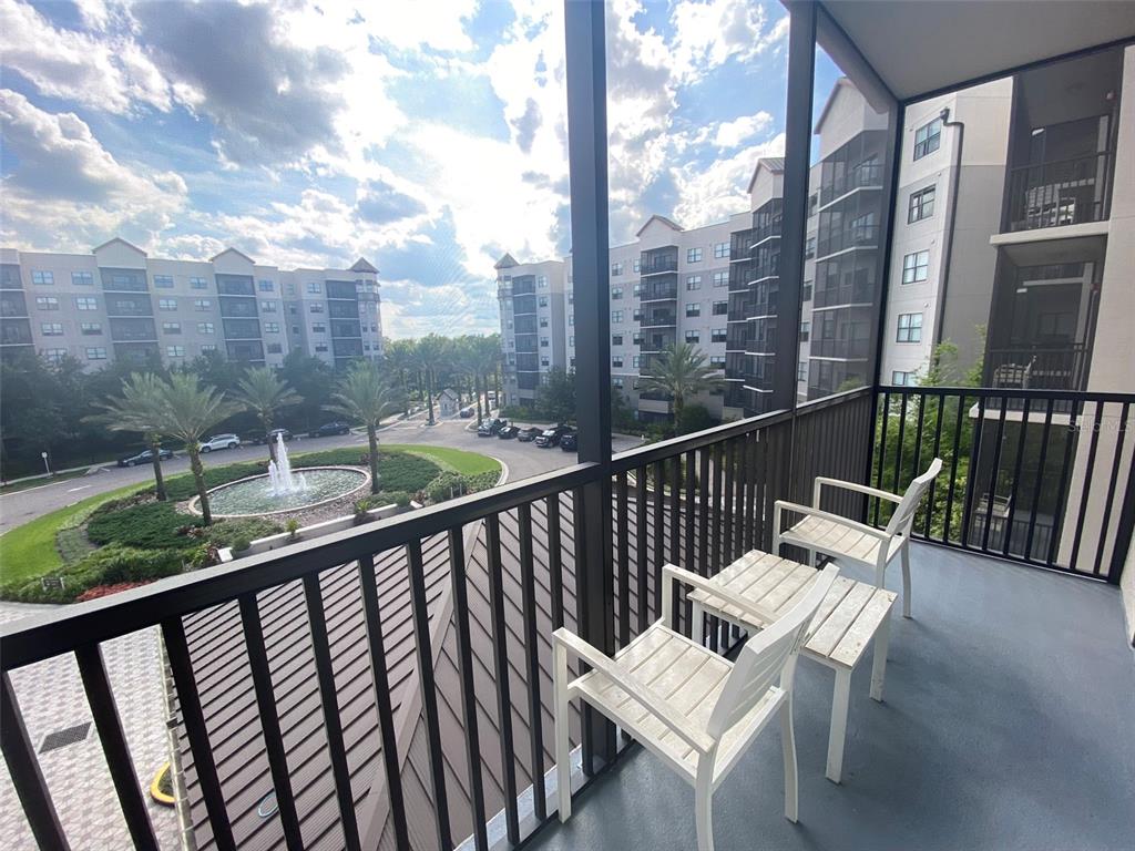 A screened-in balcony features two white chairs, a small table, and a fountain view — 14501 GROVE RESORT AVENUE UNIT 1439, WINTER GARDEN, FL