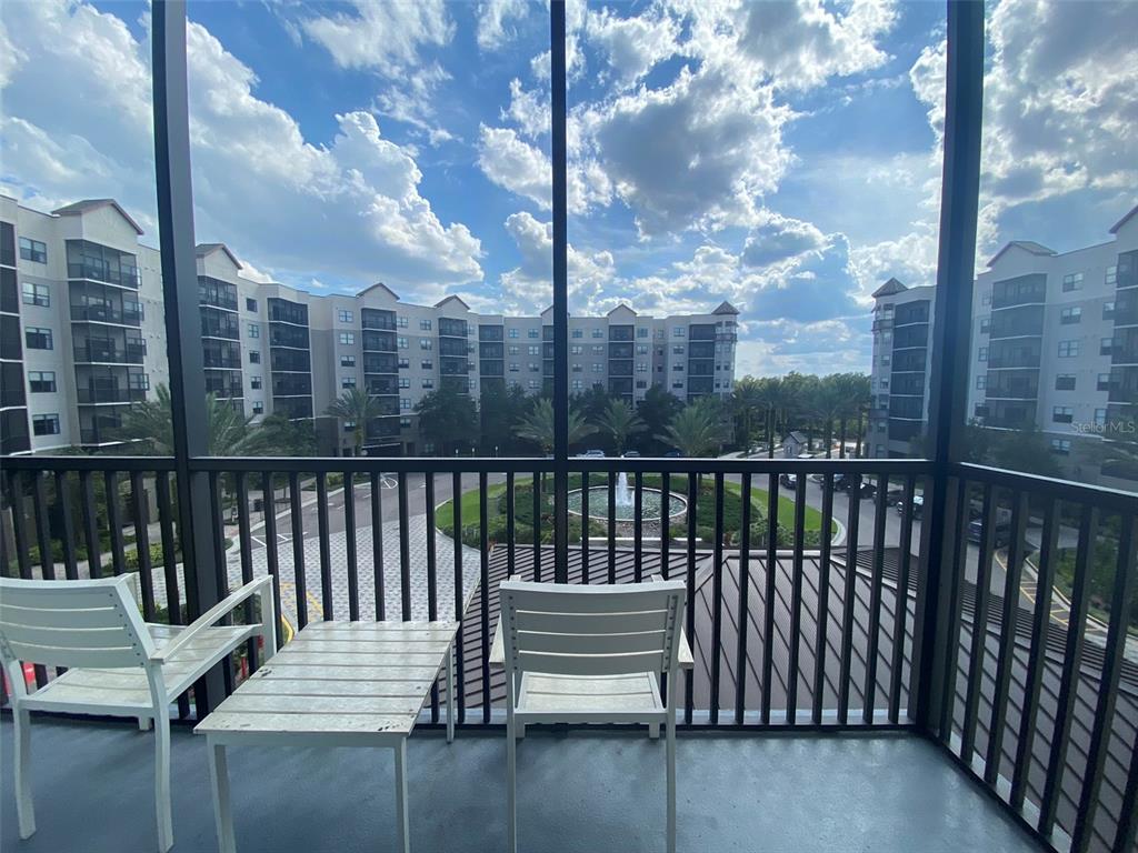 A screened balcony features white chairs and a table overlooking a courtyard with a fountain — 14501 GROVE RESORT AVENUE UNIT 1439, WINTER GARDEN, FL