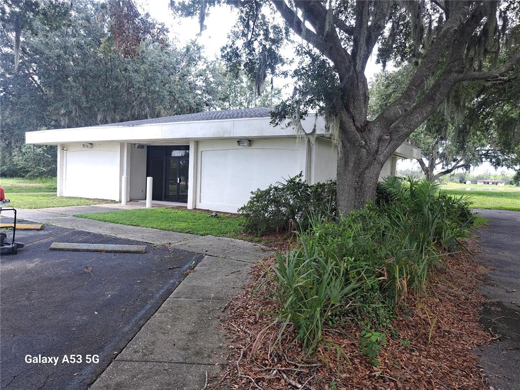 A single-story commercial building with a flat roof, white exterior, and a large oak tree — 6481 DELAND AVENUE, INDIAN LAKE ESTATES, FL