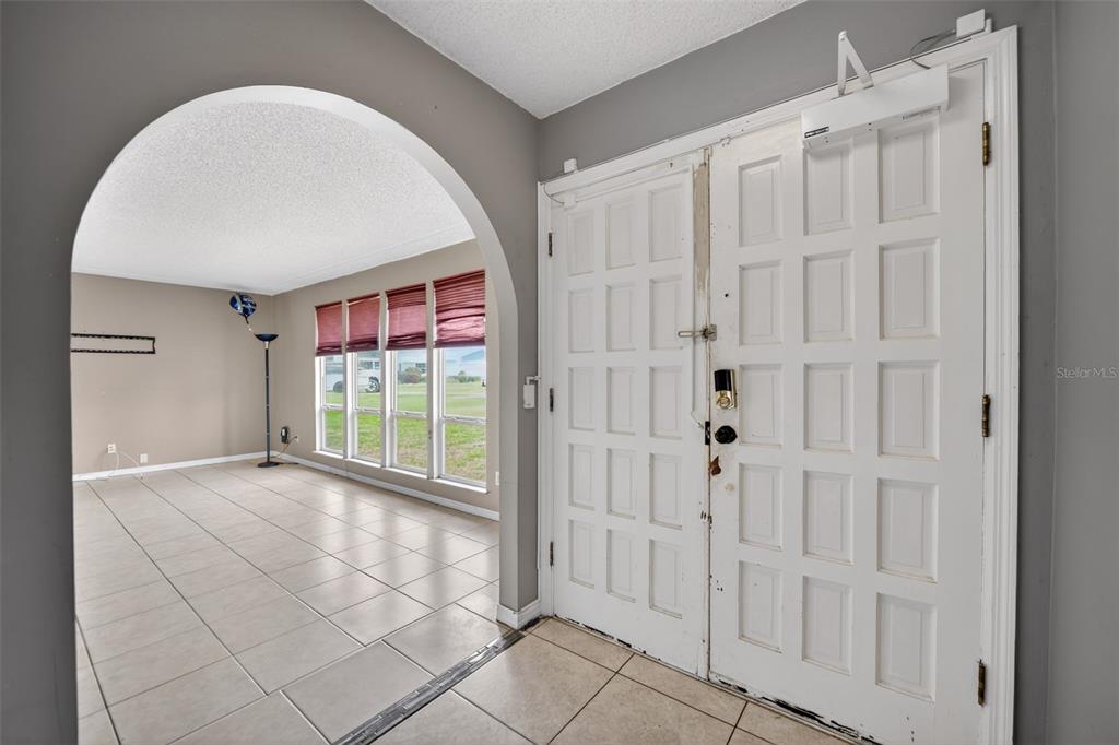 An entryway with tile flooring leads through an arched opening into a sunlit living room — 175 SHERIDAN AVENUE, LONGWOOD, FL