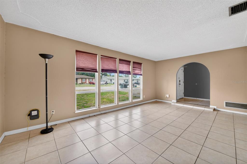 An empty room with beige walls, tile flooring, large windows, and an arched entryway — 175 SHERIDAN AVENUE, LONGWOOD, FL