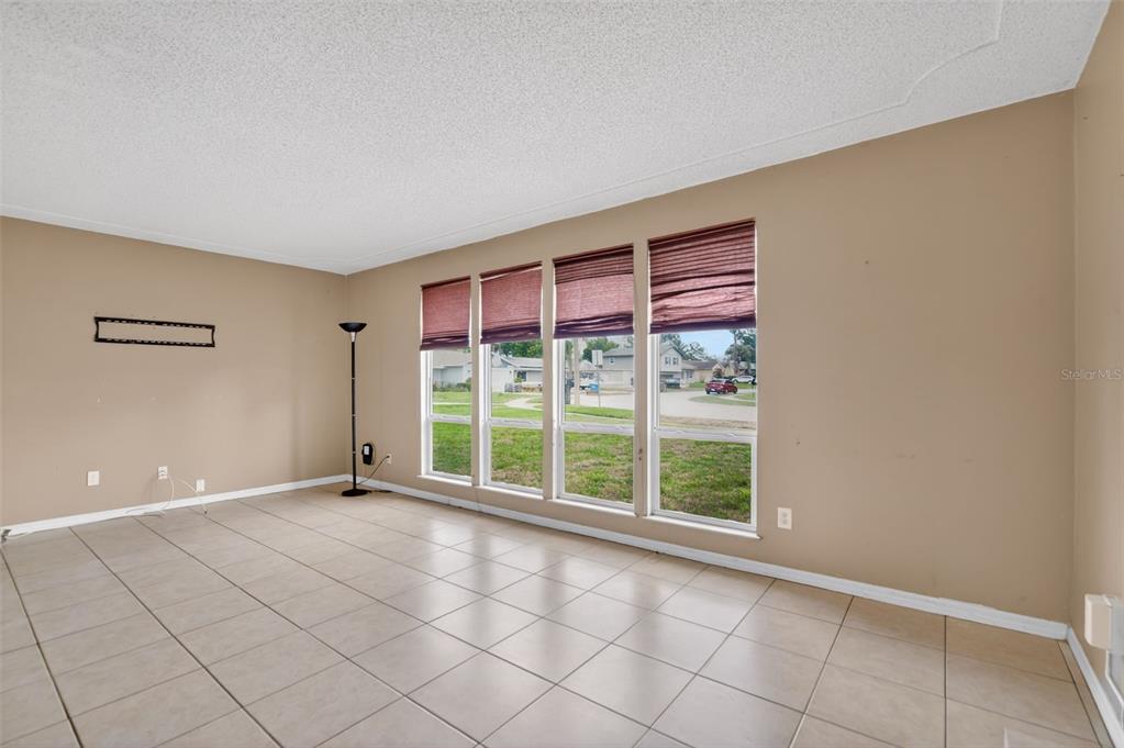 An empty room features beige walls, light-colored tile flooring, and four large windows with blinds — 175 SHERIDAN AVENUE, LONGWOOD, FL