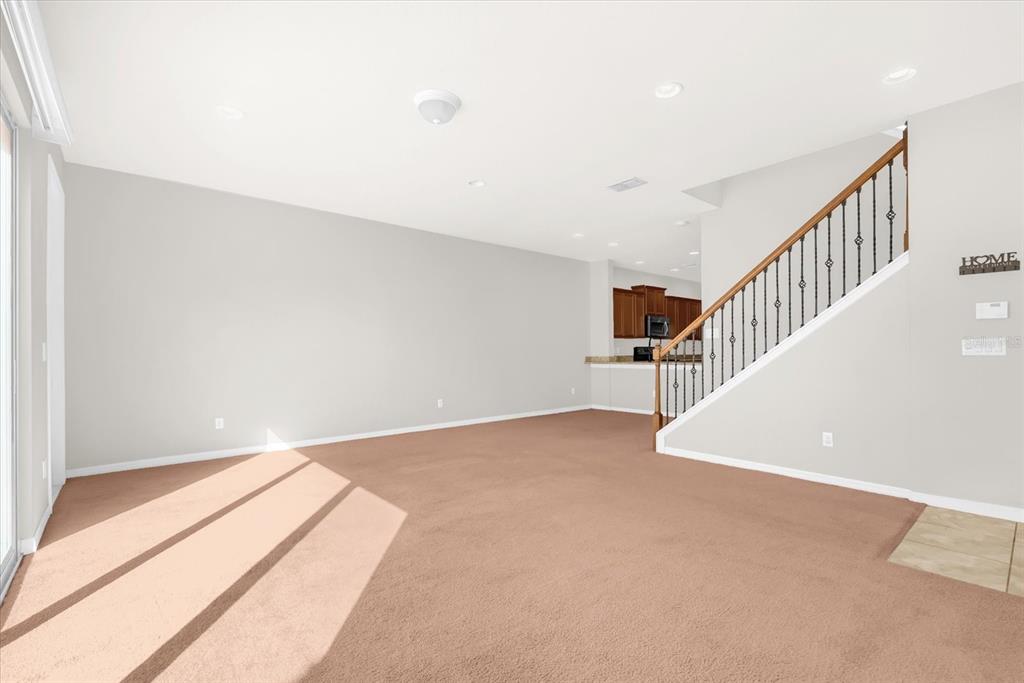 An open-concept living area features beige carpeting, light gray walls, and a wooden staircase — 11932 LORENZA LANE, ORLANDO, FL