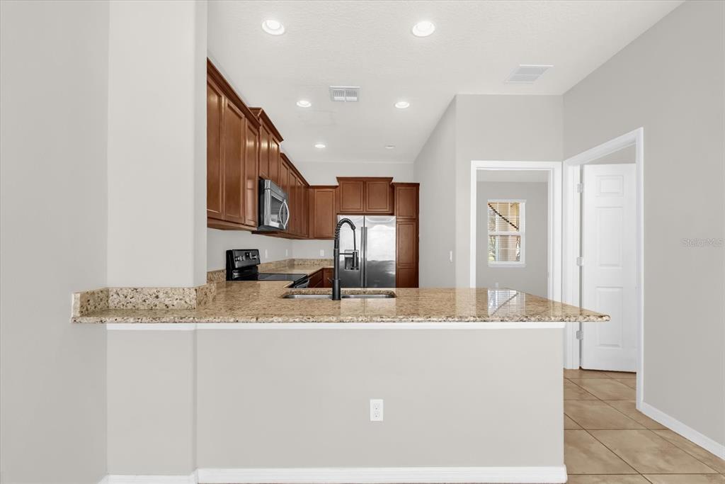 A kitchen features dark wood cabinets, granite countertops, and a breakfast bar overlooking the room — 11932 LORENZA LANE, ORLANDO, FL