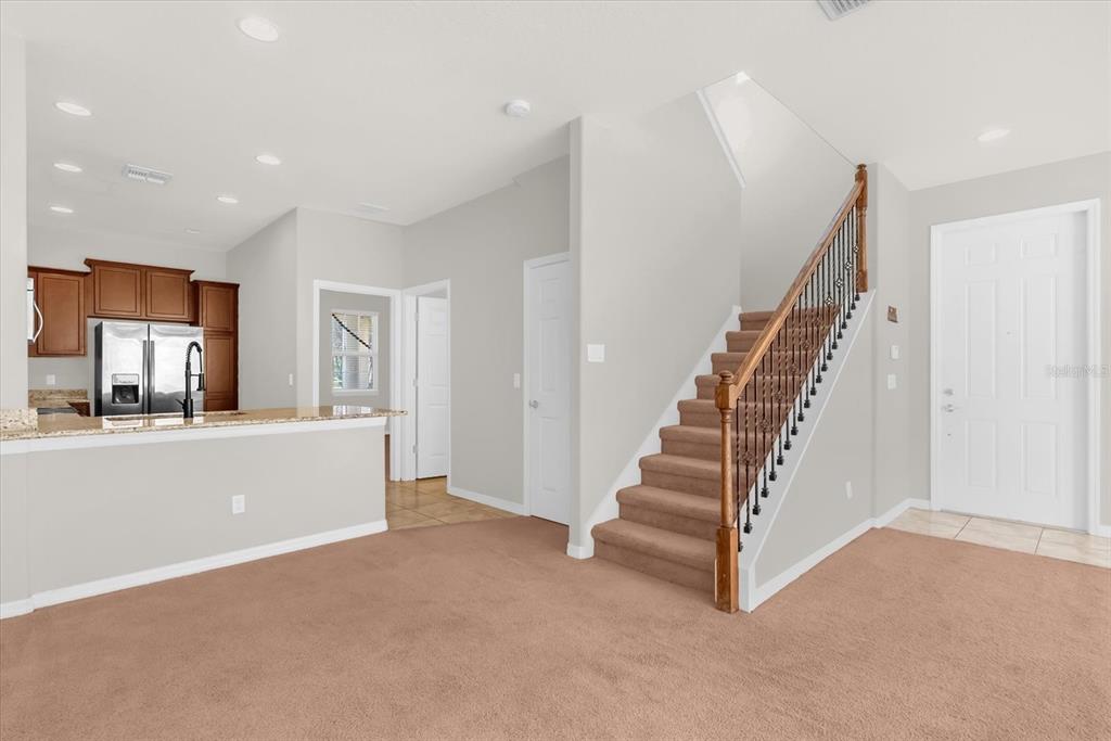 A carpeted living area features a staircase with a metal railing and an adjacent kitchen — 11932 LORENZA LANE, ORLANDO, FL