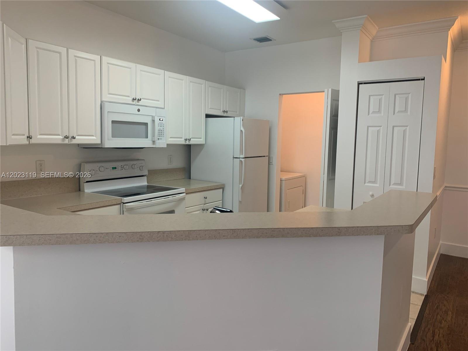 A kitchen features white cabinets, white appliances, and a beige countertop with a breakfast bar — 4702 SW 160th Ave # 325, Miramar FL 33027, MIRAMAR, FL