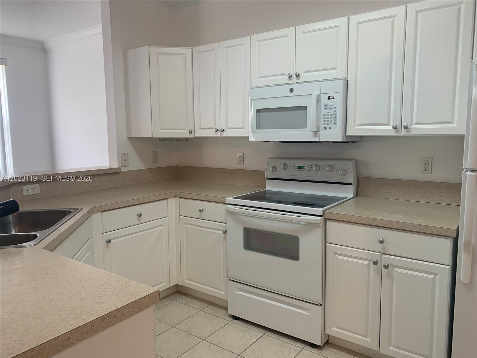 A kitchen features white cabinets, tan countertops, and white appliances — 4702 SW 160th Ave # 325, Miramar FL 33027, MIRAMAR, FL