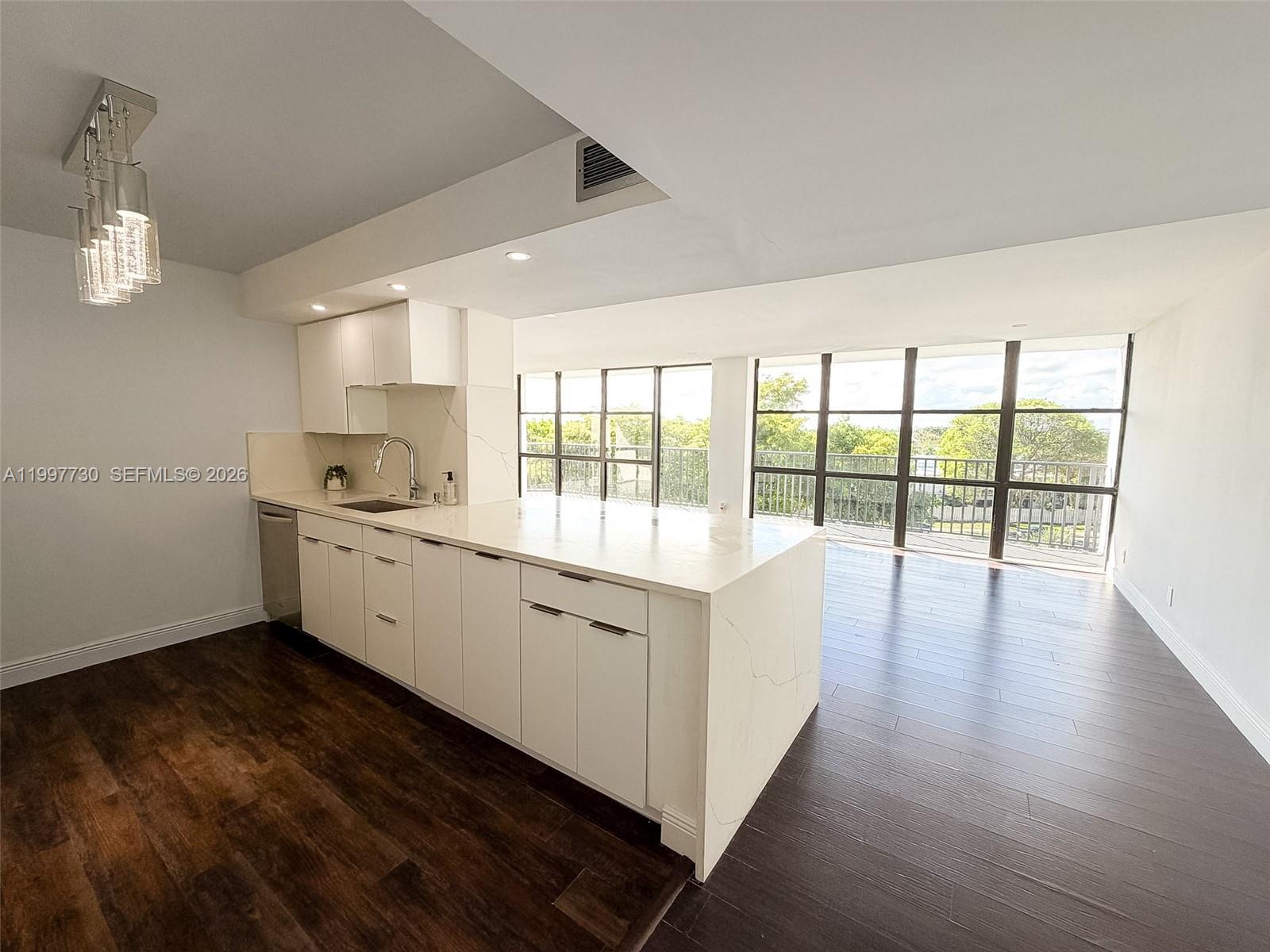 A modern kitchen features white cabinetry, quartz countertops, and dark wood flooring with floor-to-ceiling windows — 1000 Parkview Dr # 531, Hallandale Beach FL 33009, HALLANDALE BEACH, FL