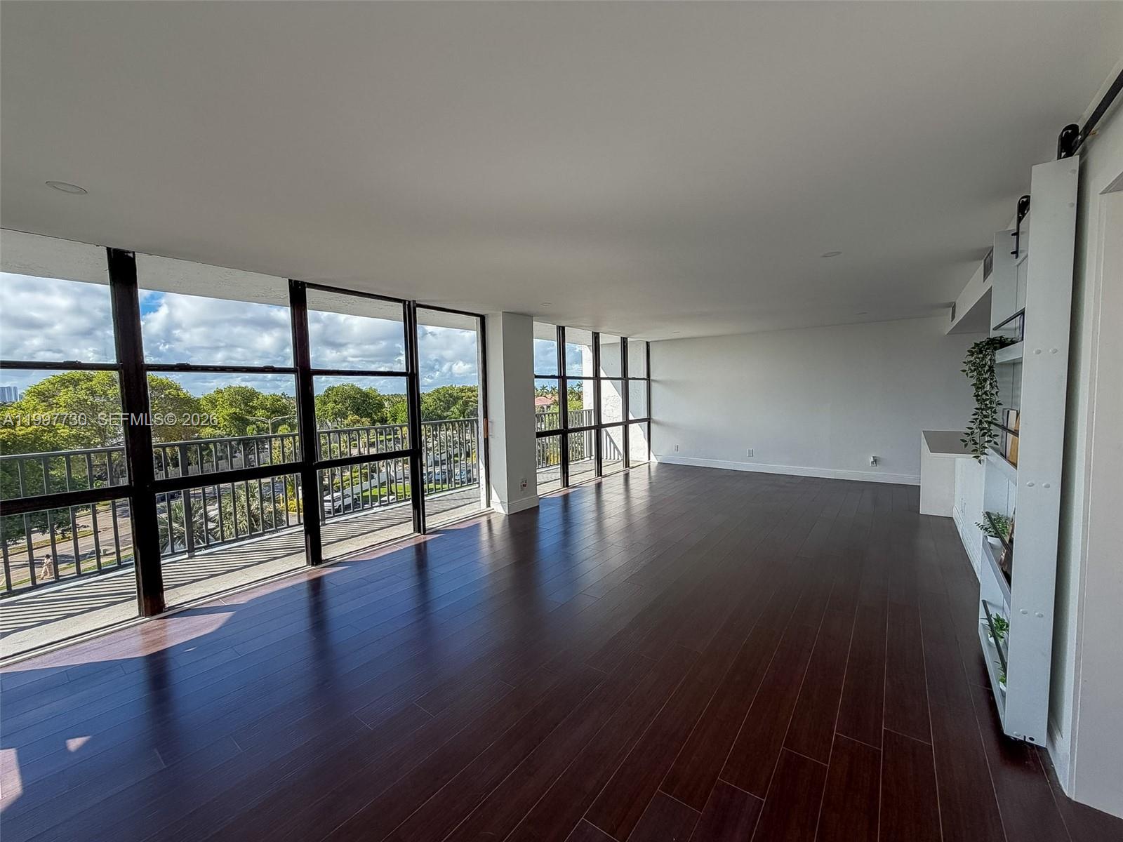 An empty room features dark wood flooring, white walls, and floor-to-ceiling windows overlooking trees — 1000 Parkview Dr # 531, Hallandale Beach FL 33009, HALLANDALE BEACH, FL