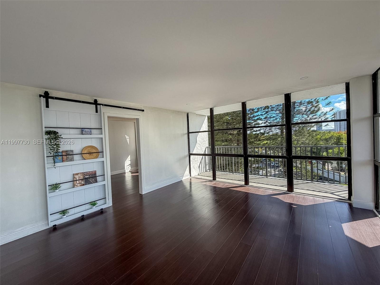 A living room features dark wood floors, a sliding barn-door bookshelf, and floor-to-ceiling windows — 1000 Parkview Dr # 531, Hallandale Beach FL 33009, HALLANDALE BEACH, FL