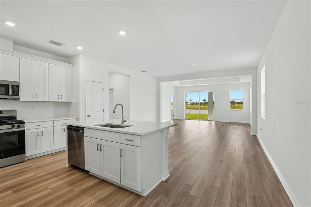 A modern kitchen with white cabinetry and a center island opens into a spacious living area — 13814 BERTRAND AVENUE, PALMETTO, FL