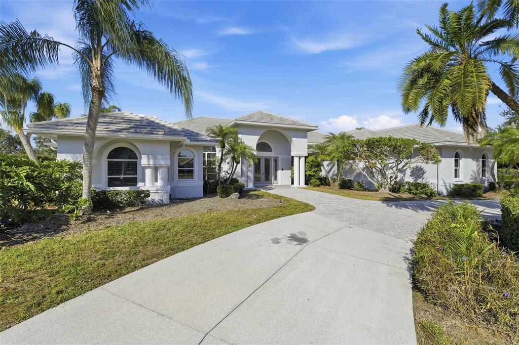 A single-story house with a concrete driveway, arched windows, and palm trees under a blue sky — 7796 ALISTER MACKENZIE DRIVE, SARASOTA, FL