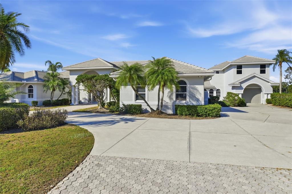 A large, light-colored single-story house with a concrete driveway and palm trees in front — 7796 ALISTER MACKENZIE DRIVE, SARASOTA, FL