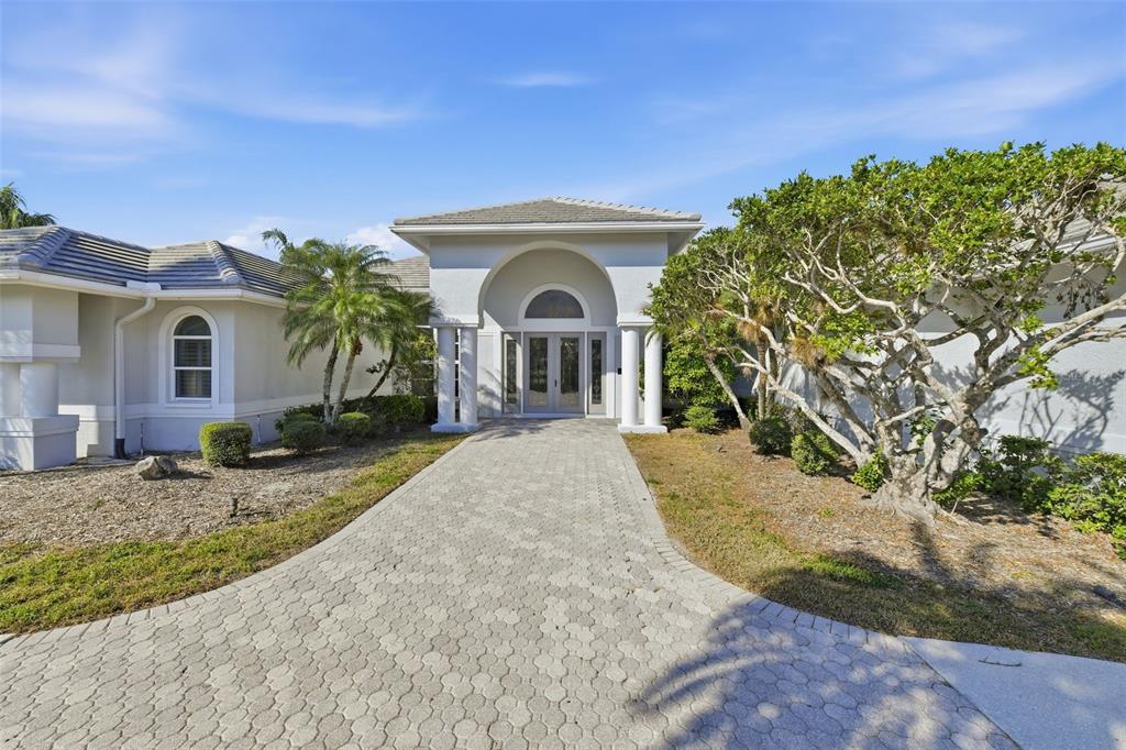 A paved walkway leads to the arched entryway of a single-story house with white stucco — 7796 ALISTER MACKENZIE DRIVE, SARASOTA, FL