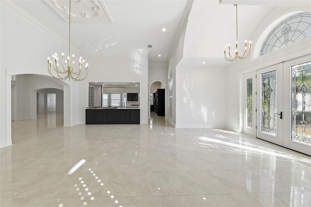 A bright, open-concept foyer features white walls, polished tile floors, and two gold chandeliers — 7796 ALISTER MACKENZIE DRIVE, SARASOTA, FL
