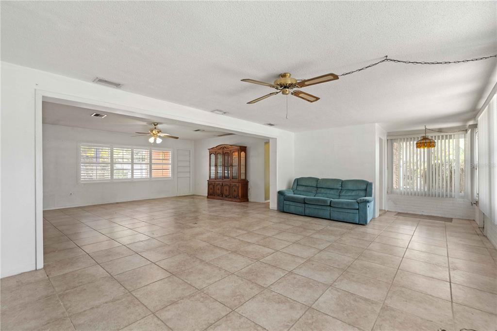 A spacious living room with tile flooring, a blue sofa, and two ceiling fans — 927 PARKWOOD DRIVE, DUNEDIN, FL