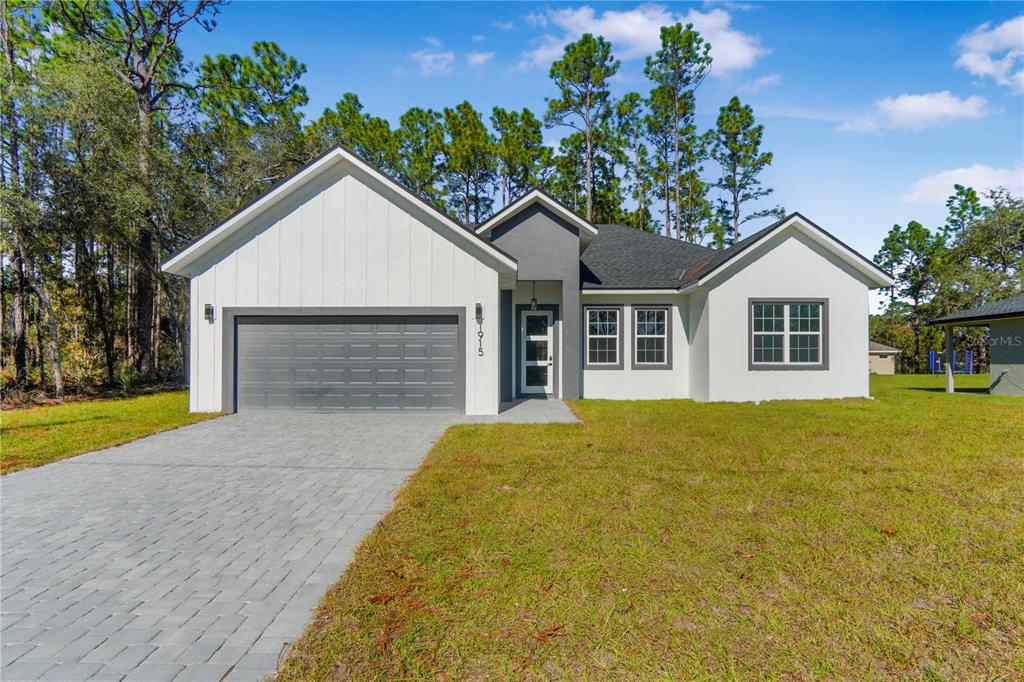 A single-story house with a white exterior, gray garage door, and a paved driveway — 1915 W LINDEN DRIVE, DUNNELLON, FL