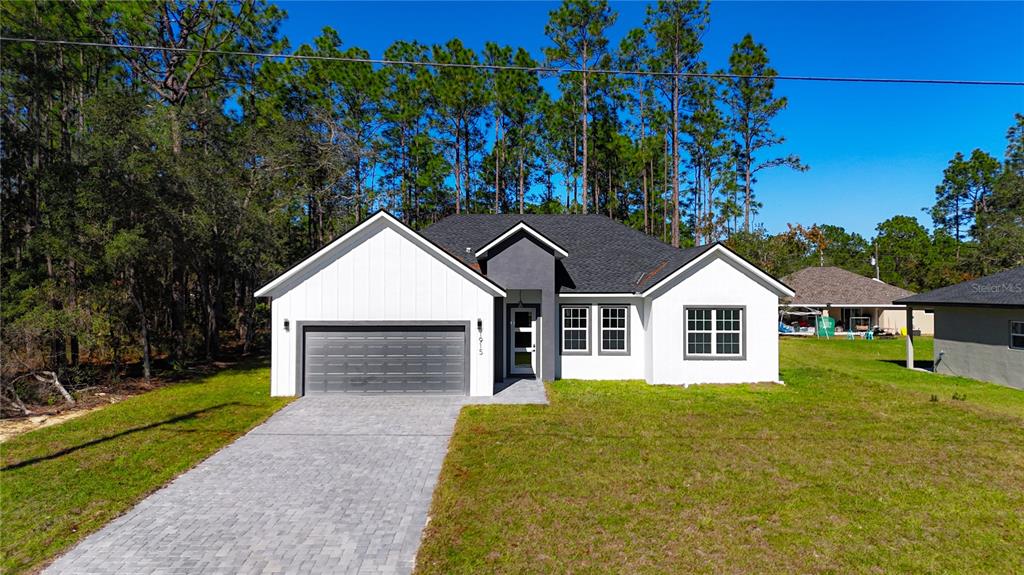 A modern single-story house with a white exterior, gray garage door, and a paved driveway — 1915 W LINDEN DRIVE, DUNNELLON, FL