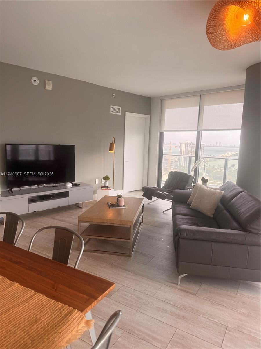A modern living room features a gray sofa, wood coffee table, and floor-to-ceiling windows — 121 NE 34th St # 1904, Miami FL 33137, MIAMI, FL