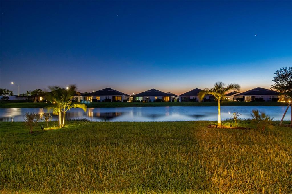 A row of houses sits across a pond at dusk with palm trees in the foreground — 18122 BEACH RANCH TERRACE, LAKEWOOD RANCH, FL