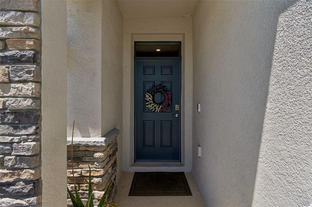 A blue front door with a wreath is set within a recessed stone-accented entryway — 18122 BEACH RANCH TERRACE, LAKEWOOD RANCH, FL