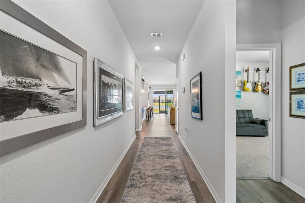 A hallway with wood-look flooring, a runner rug, and framed artwork leads toward a living area — 18122 BEACH RANCH TERRACE, LAKEWOOD RANCH, FL