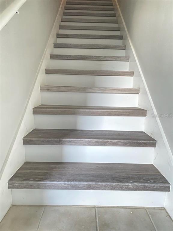 A staircase with wood-look treads and white risers leads upward between two plain walls — 142 SOUTHERN PECAN CIRCLE UNIT 204, WINTER GARDEN, FL