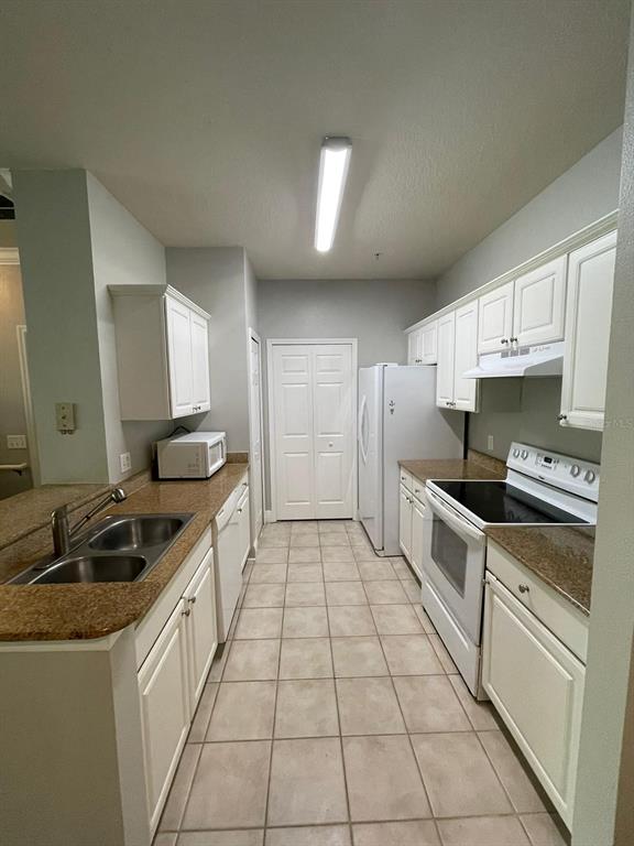 A kitchen features white cabinets, granite countertops, tile flooring, and white appliances — 142 SOUTHERN PECAN CIRCLE UNIT 204, WINTER GARDEN, FL