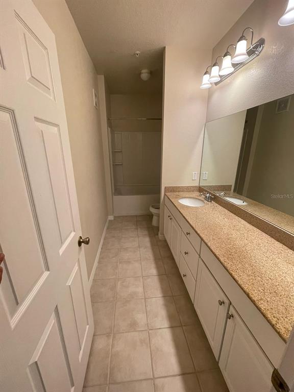 A bathroom features a long vanity with a granite countertop, white cabinets, and tile flooring — 142 SOUTHERN PECAN CIRCLE UNIT 204, WINTER GARDEN, FL