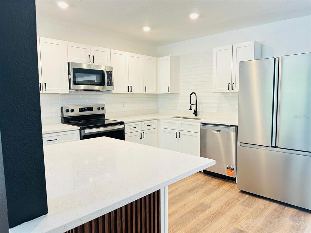 A modern kitchen features white cabinets, stainless steel appliances, and a white quartz island countertop — 5621 LEJEUNE DRIVE, ORLANDO, FL