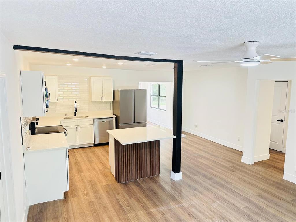 A modern kitchen with white cabinets, stainless steel appliances, and a wood-paneled island — 5621 LEJEUNE DRIVE, ORLANDO, FL
