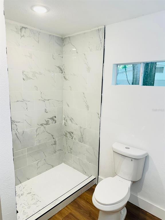 A bathroom features a walk-in shower with marble-look tile, a white toilet, and wood-look flooring — 5621 LEJEUNE DRIVE, ORLANDO, FL