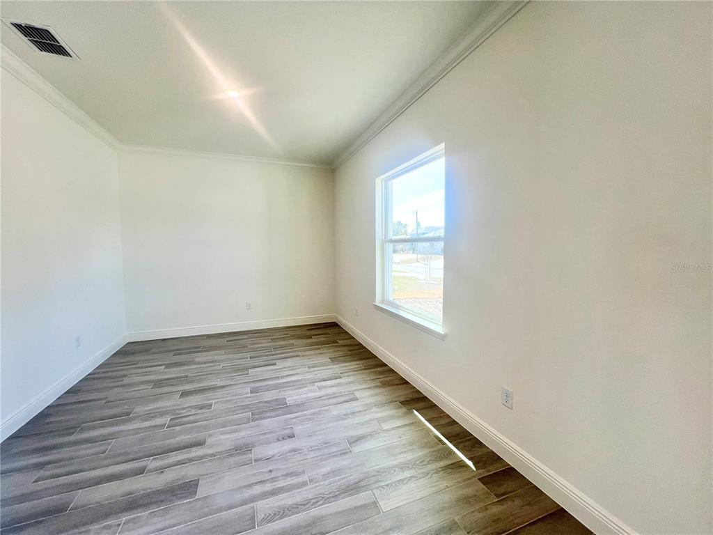 An empty room features white walls, crown molding, and gray wood-look tile flooring — 31 FALLEN OAK LANE, PALM COAST, FL