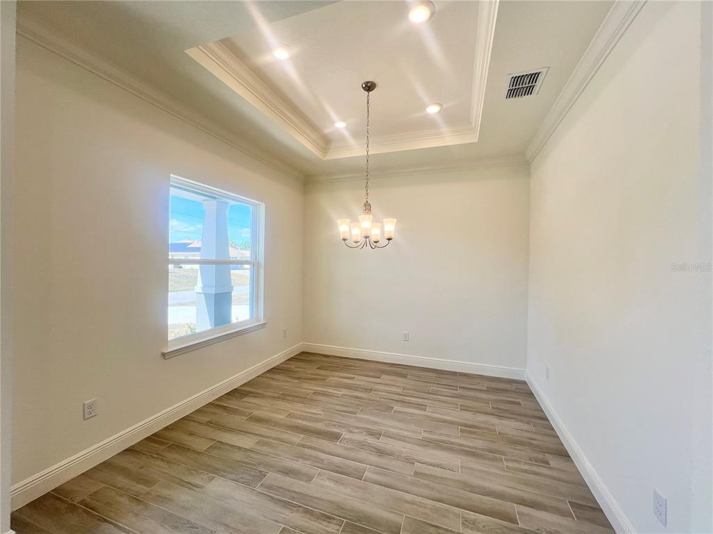 A dining room features a tray ceiling, a chandelier, and light wood-look tile flooring — 31 FALLEN OAK LANE, PALM COAST, FL
