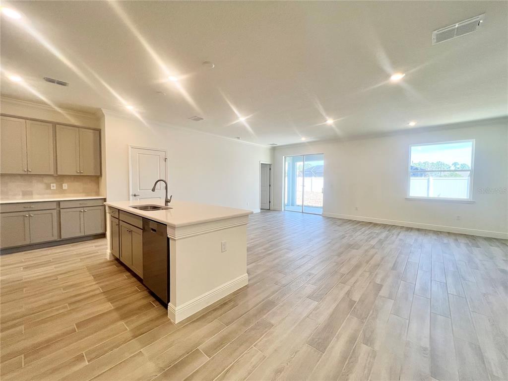 A modern kitchen with gray cabinets and a white island opens into a spacious living area — 31 FALLEN OAK LANE, PALM COAST, FL