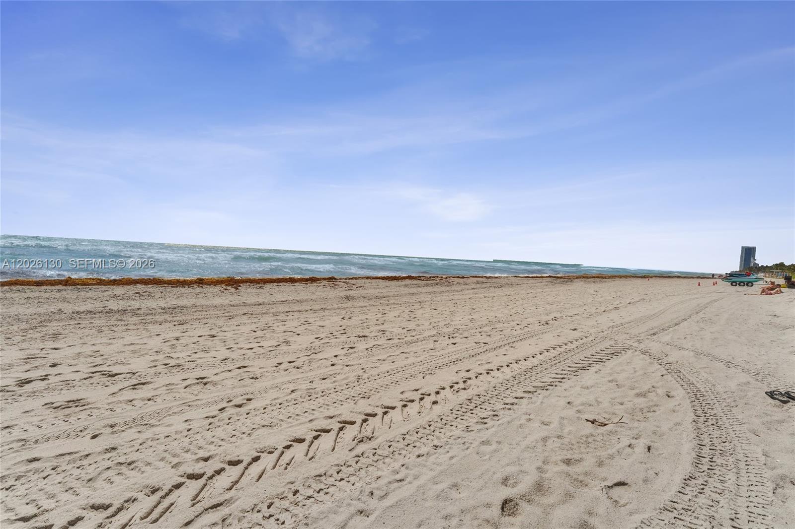 A wide, sandy beach features tire tracks leading toward the ocean under a blue sky — 1936 S Ocean Dr # 4C, Hallandale Beach FL 33009, HALLANDALE BEACH, FL