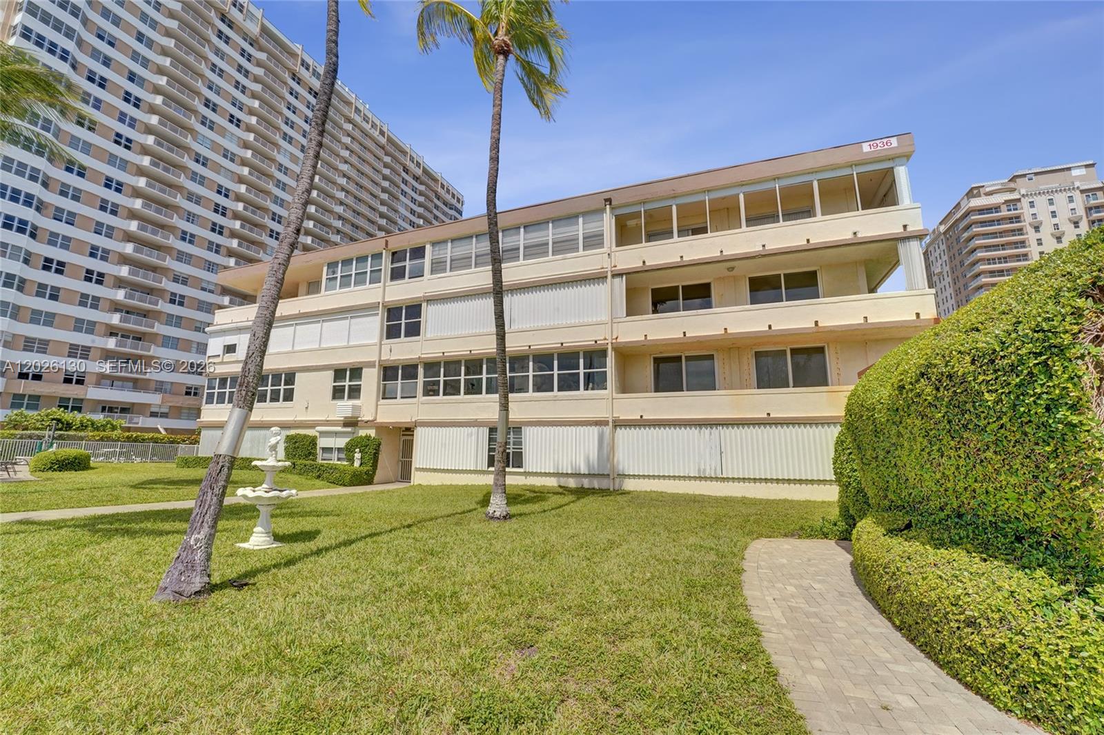 A three-story apartment building with balconies stands beside a lawn with palm trees — 1936 S Ocean Dr # 4C, Hallandale Beach FL 33009, HALLANDALE BEACH, FL