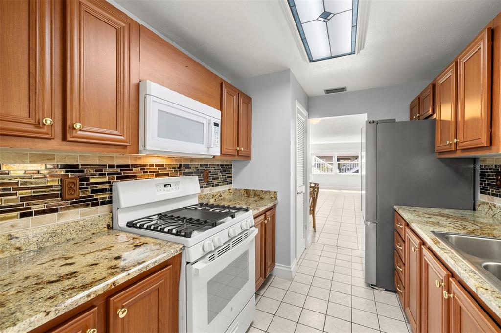 A kitchen with wood cabinets, granite countertops, a white gas stove, and a tile floor — 10038 62ND TERRACE N UNIT 1, ST PETERSBURG, FL