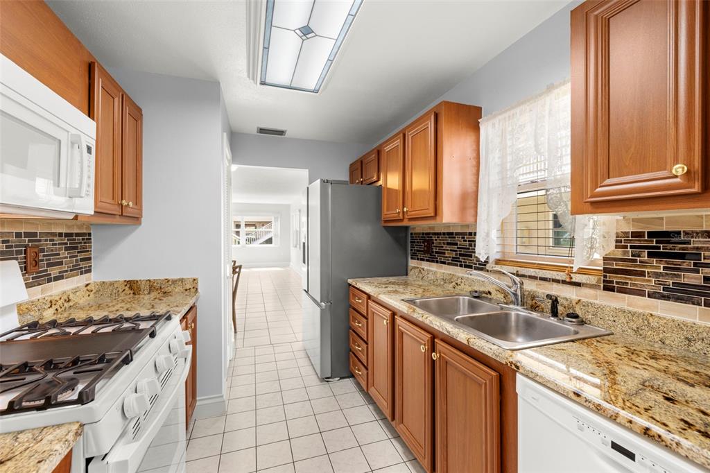 A kitchen features wood cabinets, granite countertops, a tiled backsplash, and stainless steel appliances — 10038 62ND TERRACE N UNIT 1, ST PETERSBURG, FL