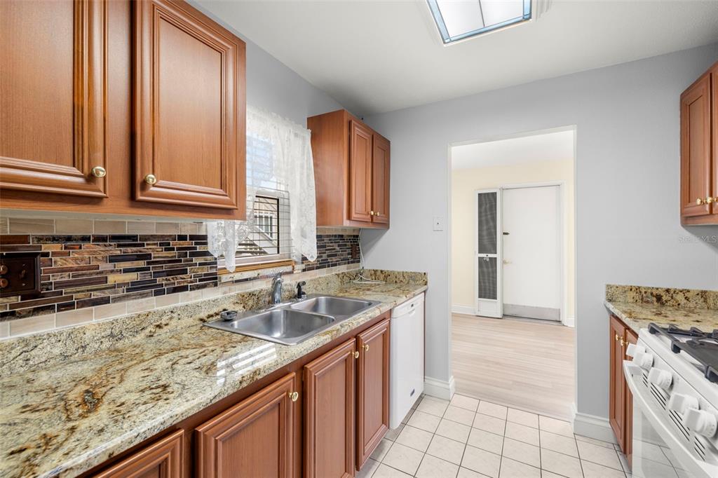 A kitchen features wood cabinets, granite countertops, a tiled backsplash, and a double sink — 10038 62ND TERRACE N UNIT 1, ST PETERSBURG, FL