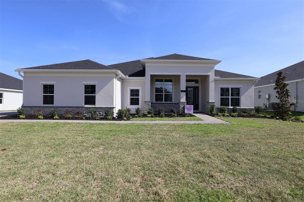 A single-story house with a beige stucco exterior, stone accents, and a dark shingled roof — 3811 WOLVES CREEK PLACE, APOPKA, FL